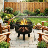 A NatureScape Living 24 Inch Wood Burning Fire Pit with a mesh screen, burning logs on a patio next to wooden chairs and firewood.