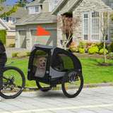 A black and gray NatureScape Living dog bike trailer with an orange safety flag holds a beagle, pulled by a bicycle.