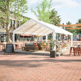 A white NatureScape Living Heavy Duty Party Tent 16x32FT is an ultimate outdoor shelter covering wooden patio furniture in a brick plaza.