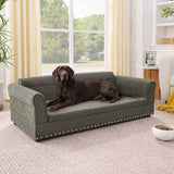 A large chocolate Labrador lies on a dark grey linen Oversized Pet Sofa with silver stud detailing in a living room.