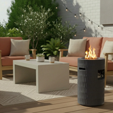 A dark grey 26" Propane Fire Pit with hidden tank storage illuminates a modern outdoor patio with seating and plants.