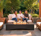 NatureScape Living's modern 56" Rectangular Gas Fire Pit Table offers a cozy outdoor escape for three friends enjoying wine on a patio.