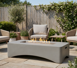 NatureScape Living's modern gray rectangular propane fire pit table with flames sits on a stone patio with wicker chairs.