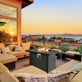 Dark wicker NatureScape Living 30 Inch Auto-Ignition Rectangular Fire Pit with fire on a patio overlooking a lake at sunset.