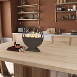 A black round bioethanol fireplace with flickering flames on a light wood kitchen table, accented by books and a diffuser.