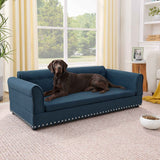 An oversized, elevated blue linen dog sofa bed with elegant stud trim, featuring a large brown dog lounging on a rug.