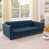 An elegant blue linen Dog Sofa Bed, featuring a tufted back, rolled arms, and silver nailhead trim, sits on a rug with a pet food bowl.