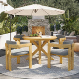NatureScape Living's 5-piece acacia wood round patio dining set with gray cushions on an outdoor patio with a fireplace.