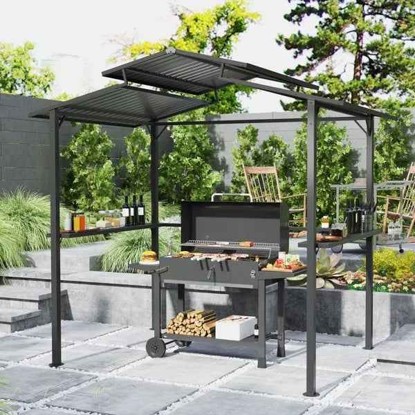 A black metal Premium Outdoor Grill Gazebo from NatureScape Living with a corrugated roof covers a grill, food, and firewood on a patio.