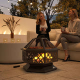 Two women enjoy a NatureScape Living 18-inch metal wood-burning fire pit with a cooking grate for outdoor entertaining.