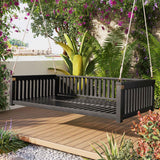 A black TOPMAx Minimalist Twin Size Garden Swing Bed with a slatted design hangs from ropes on a wooden deck in a lush garden.