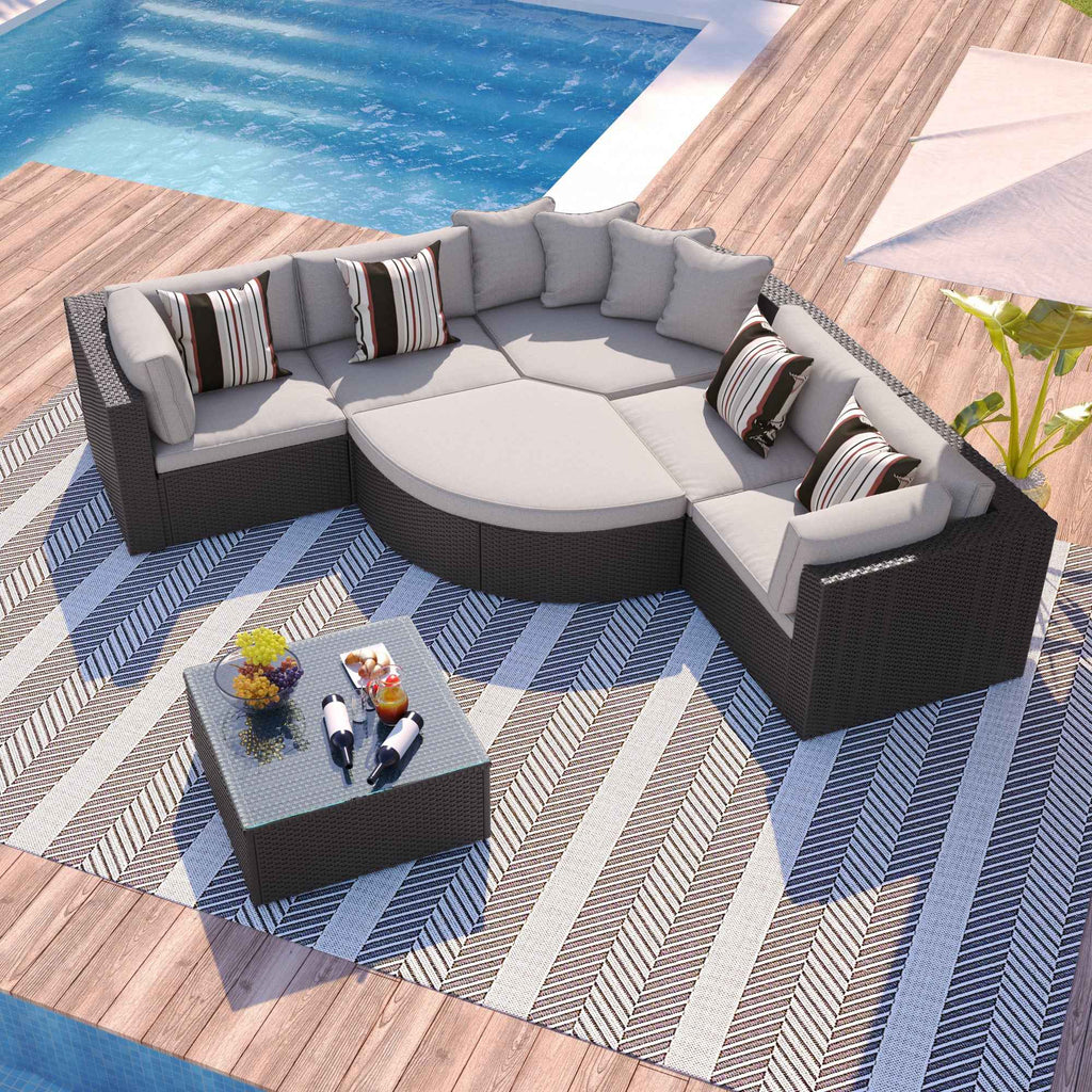 GO 7-piece brown rattan lounger with beige cushions and striped pillows on a striped rug by a pool.