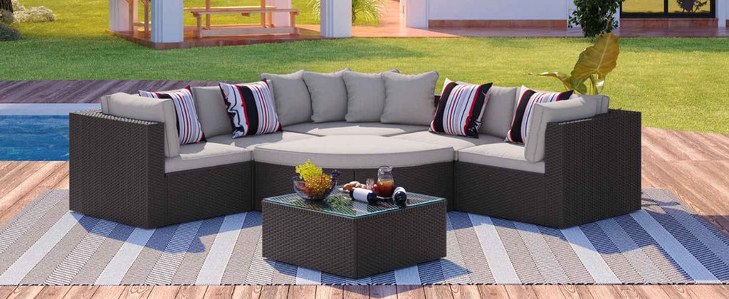 A GO 7-piece brown wicker outdoor sofa set with beige cushions, striped pillows, and coffee table on a deck by a pool.