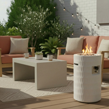 A 26" modern white Propane Patio Fire Pit with textured sides emits flames on a deck with outdoor seating.
