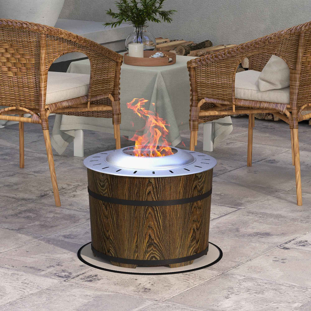 A NatureScape Living Smokeless Fire Pit, with a wood barrel base and silver top, brightly burning on a patio between two wicker chairs.