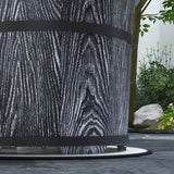 A black smokeless fire pit with a wood-grain texture and banding sits on a white mat in an outdoor garden setting.
