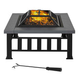 A dark gray steel NatureScape Living 34" square wood burning fire pit table with a glowing fire, a mesh cover, and a fire poker.