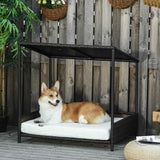 A Corgi dog relaxes on the white cushion of a dark brown raised rattan puppy bed with a canopy, set on an outdoor deck.