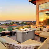 A grey NatureScape Living Wicker Propane Fire Pit Table provides warmth for outdoor entertaining on a patio at sunset.