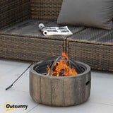 Outsunny 18-inch wood burning fire pit with a rustic, stump-like design, burning brightly on a patio next to an outdoor sofa.