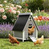 A gray wooden chicken coop with a black roof and ramp, in a garden with lavender, roses, and tulips, is surrounded by three happy hens.